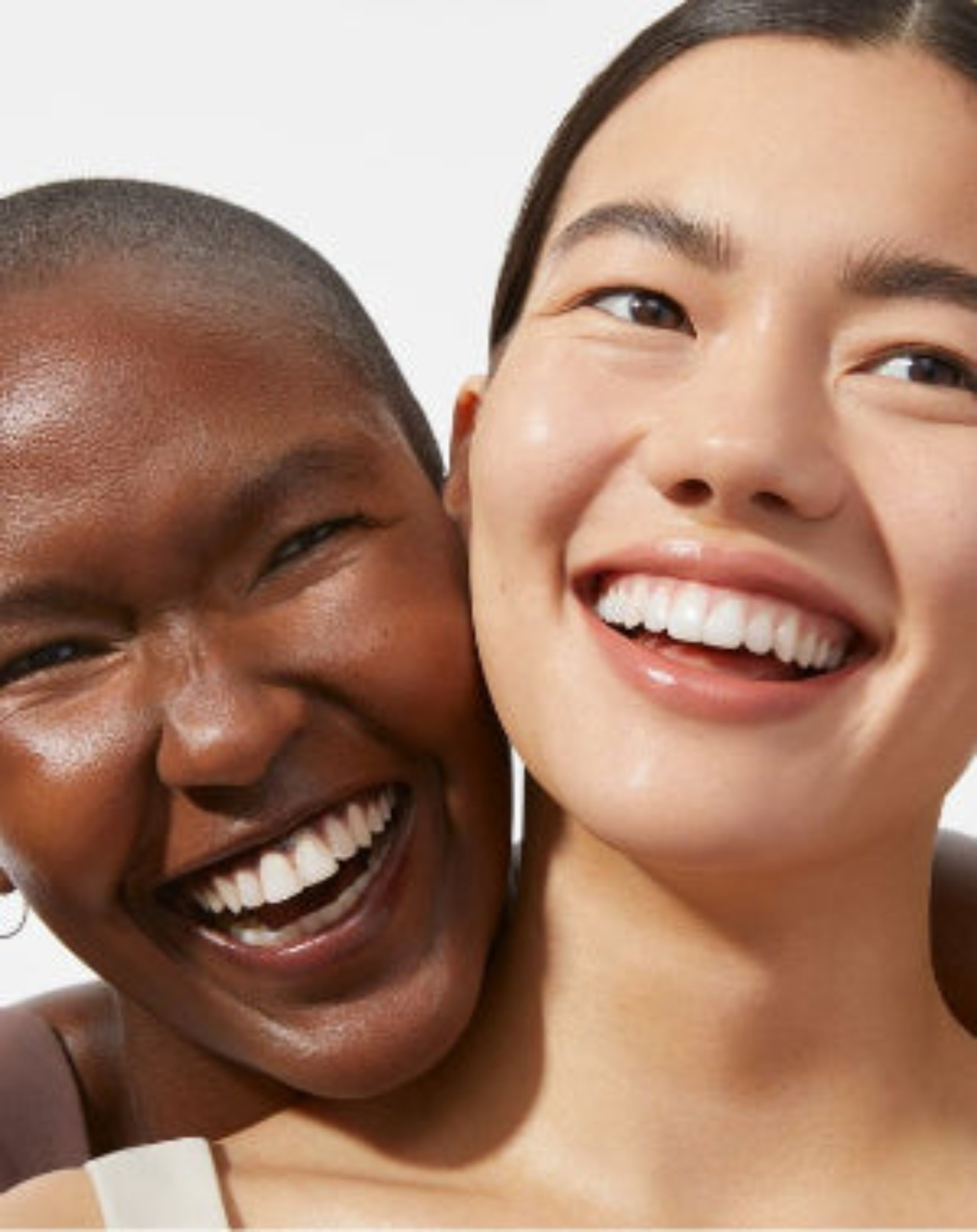 image depicting radiant skin, two women from differing ethnicities smiling brightly, example of glowing skin